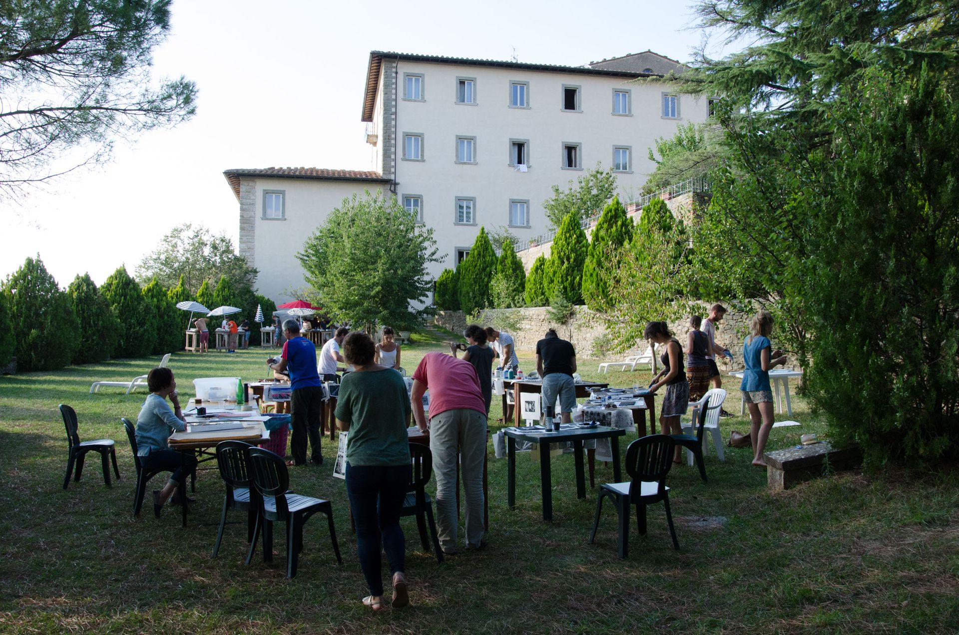 Participants work at outdoor tables during an artistic workshop beside the Cortona venue.